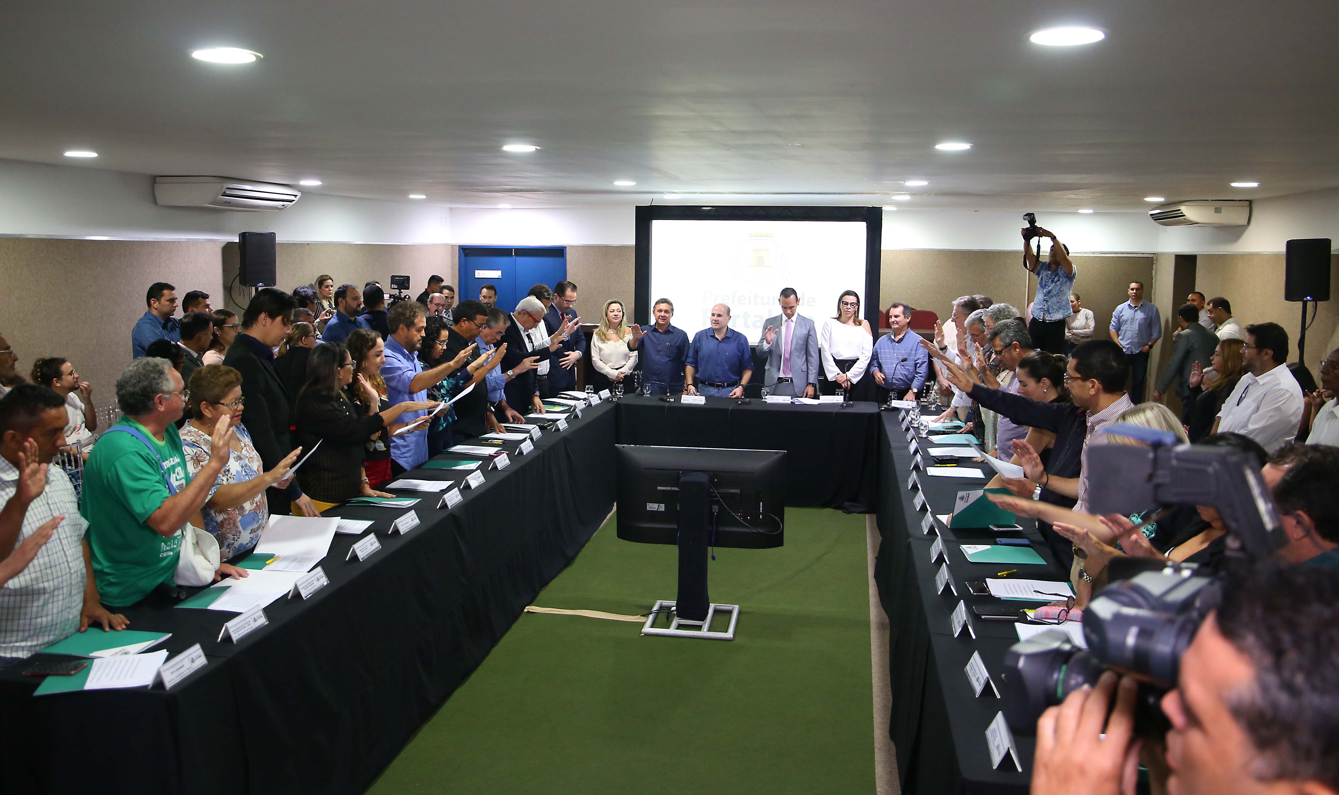 interior do auditório do paço municipal com várias pessoas sentadas em uma mesa de reunião